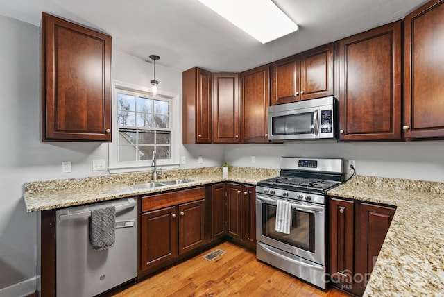 kitchen featuring light stone counters, stainless steel appliances, visible vents, light wood-style floors, and a sink