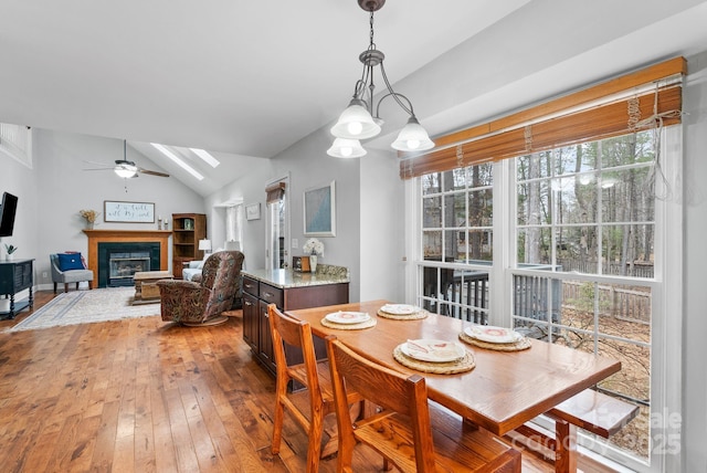 dining space featuring light wood-style floors, a glass covered fireplace, vaulted ceiling with skylight, and a ceiling fan