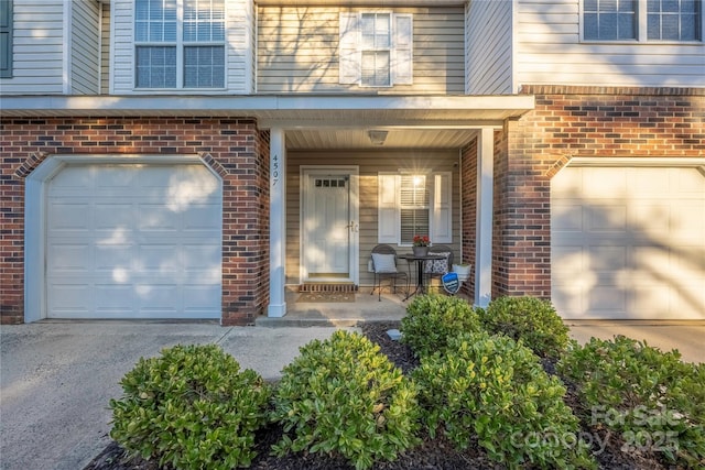 entrance to property featuring a garage, driveway, and brick siding