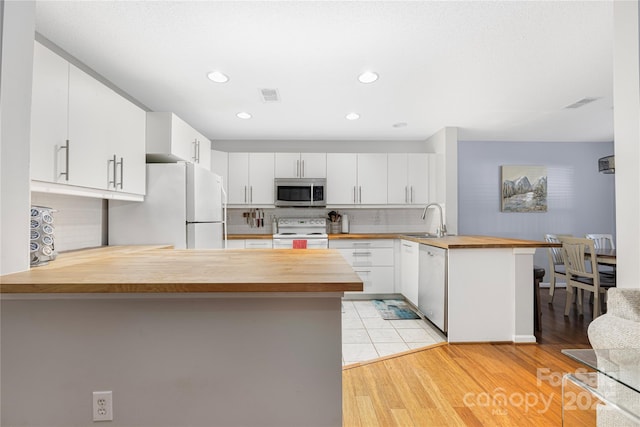 kitchen with a peninsula, butcher block counters, a sink, appliances with stainless steel finishes, and decorative backsplash