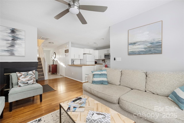 living area featuring visible vents, baseboards, a ceiling fan, stairway, and light wood-type flooring