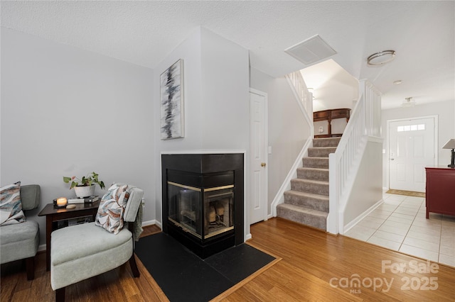 living area featuring a textured ceiling, wood finished floors, a multi sided fireplace, baseboards, and stairs