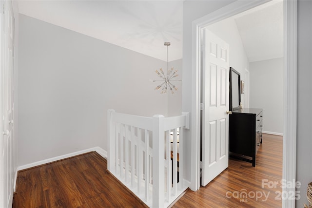 hall with baseboards, wood finished floors, an upstairs landing, and an inviting chandelier