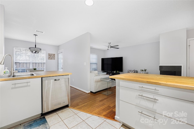 kitchen with light tile patterned floors, a sink, visible vents, wood counters, and stainless steel dishwasher