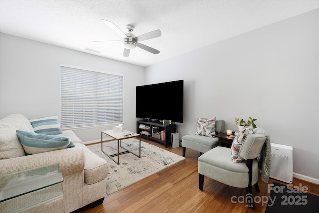 living area with ceiling fan, wood finished floors, visible vents, and baseboards