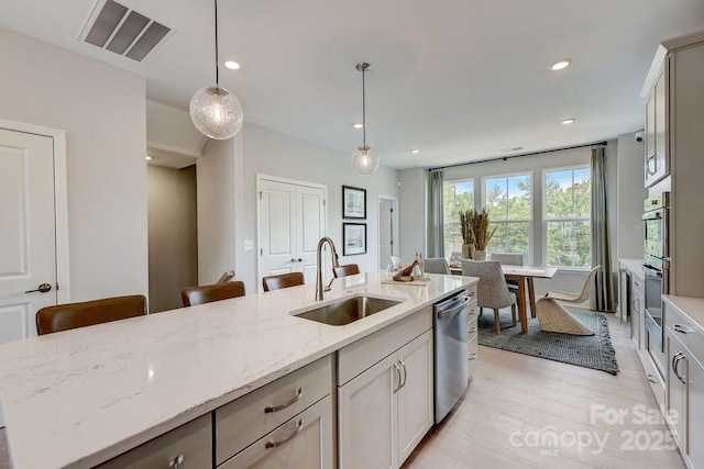 kitchen featuring visible vents, a sink, light wood finished floors, light stone countertops, and stainless steel dishwasher
