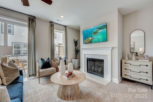 living room with visible vents, baseboards, ceiling fan, light wood-style floors, and a high end fireplace