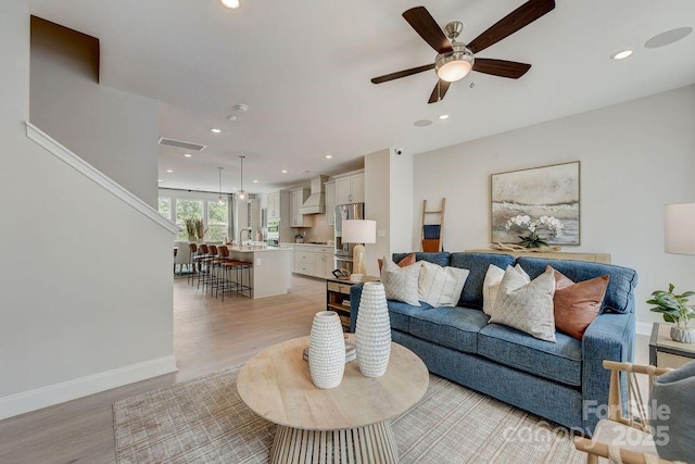 living room featuring light wood-type flooring, ceiling fan, baseboards, and recessed lighting