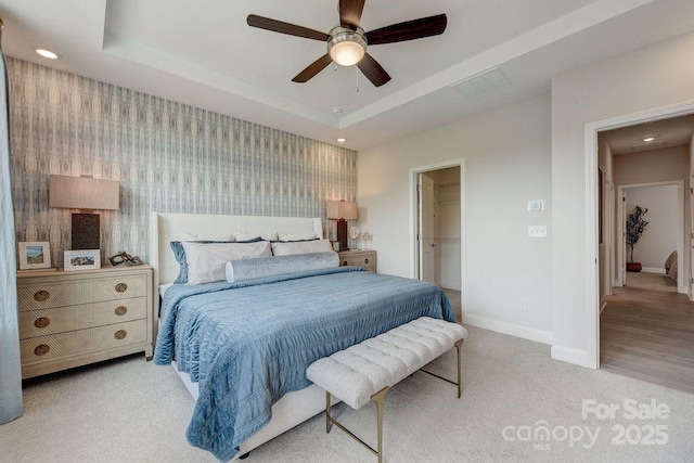 carpeted bedroom featuring baseboards, wallpapered walls, a spacious closet, recessed lighting, and a tray ceiling