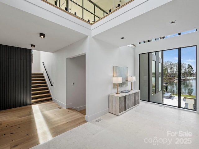 interior space with visible vents, a water view, stairway, a towering ceiling, and baseboards