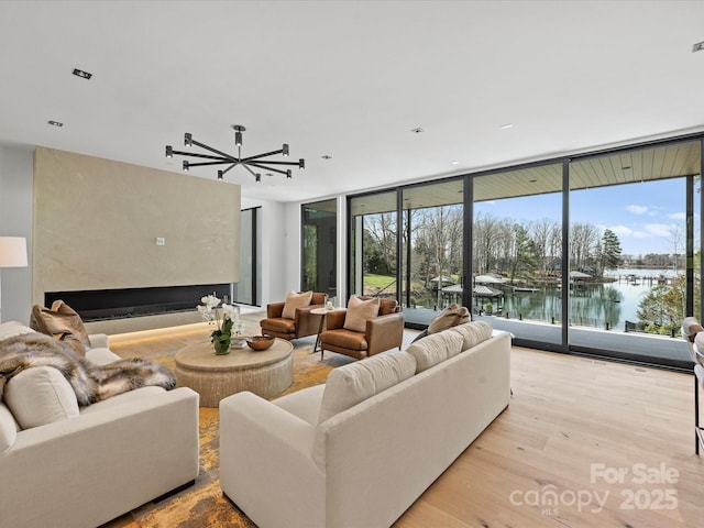 living area featuring a fireplace, a wealth of natural light, a water view, expansive windows, and light wood-type flooring