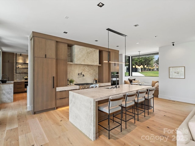 kitchen featuring decorative light fixtures, a center island with sink, light countertops, modern cabinets, and a kitchen bar