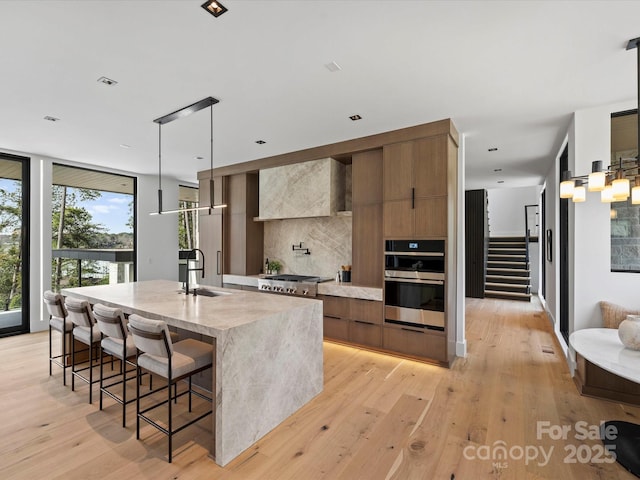 kitchen with a breakfast bar area, a kitchen island with sink, light countertops, modern cabinets, and pendant lighting