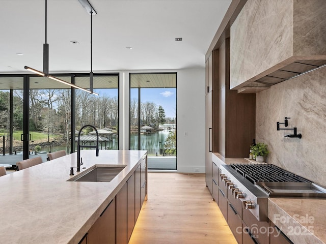 kitchen featuring a water view, premium range hood, stainless steel gas stovetop, pendant lighting, and a sink