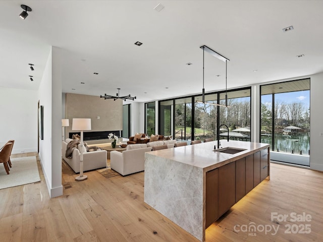 kitchen featuring a wall of windows, a water view, a center island with sink, and light wood-style floors