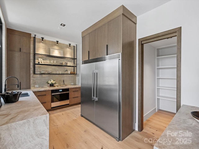 kitchen with wall oven, modern cabinets, stainless steel built in refrigerator, light countertops, and a sink