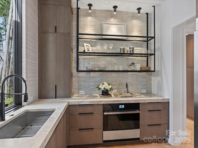 bar featuring decorative light fixtures, stainless steel oven, backsplash, and a sink