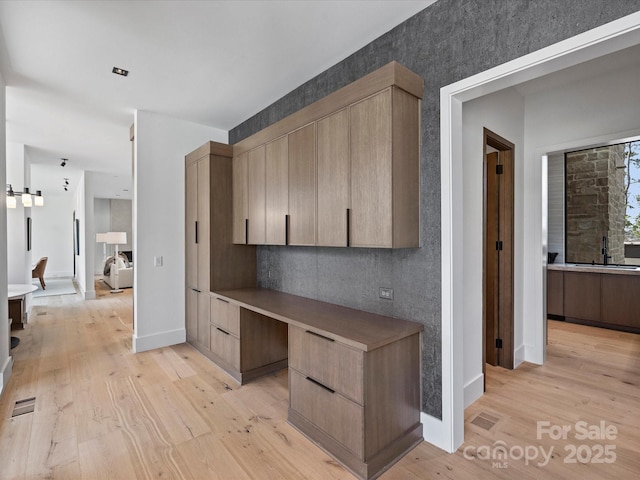 interior space featuring light wood-style floors, a sink, built in desk, and baseboards