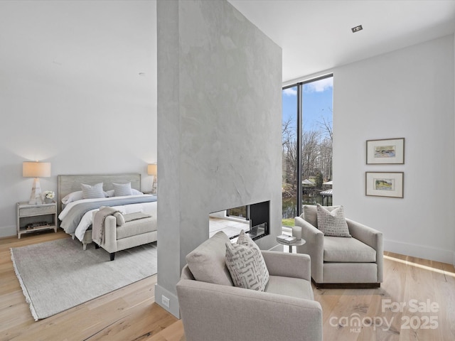 bedroom with baseboards, light wood-style floors, a high end fireplace, and floor to ceiling windows