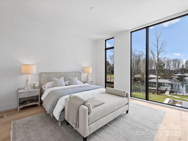 bedroom with a water view, wood finished floors, baseboards, access to exterior, and a wall of windows