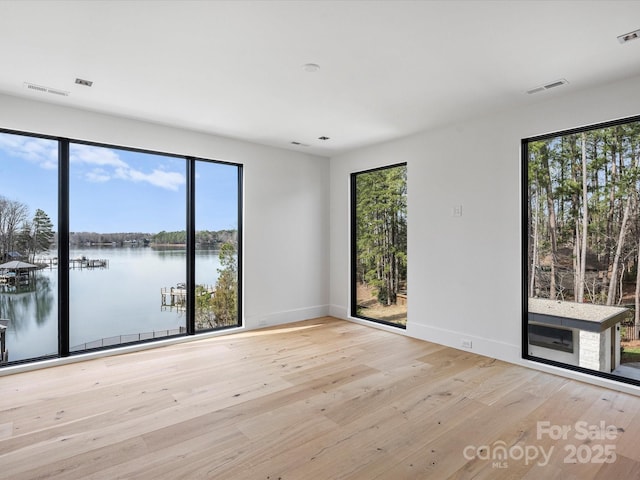 empty room with light wood-style floors, a water view, visible vents, and baseboards