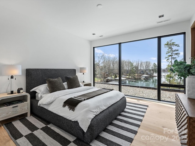 bedroom with a water view, visible vents, and light wood finished floors