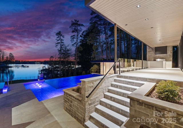 outdoor pool with a patio, exterior kitchen, and a water view