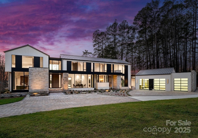 back of house featuring a lawn, stone siding, metal roof, an outbuilding, and a standing seam roof