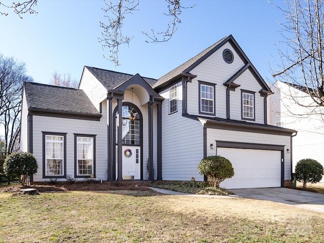 traditional home featuring an attached garage, a shingled roof, concrete driveway, and a front yard