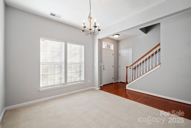 entrance foyer featuring visible vents, dark carpet, a chandelier, baseboards, and stairs