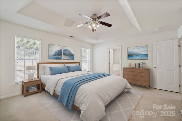 bedroom with a tray ceiling, light colored carpet, and multiple windows