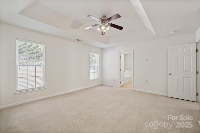 unfurnished bedroom with light carpet, visible vents, baseboards, a raised ceiling, and connected bathroom