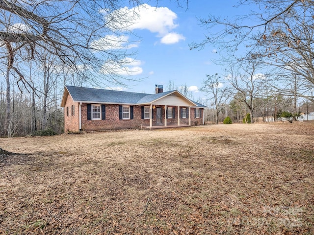 single story home with covered porch, brick siding, a chimney, and a front lawn