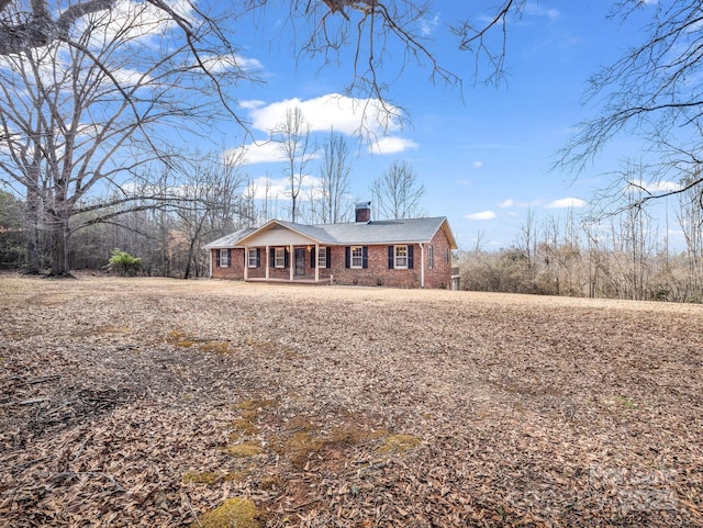 single story home featuring covered porch, brick siding, and a chimney