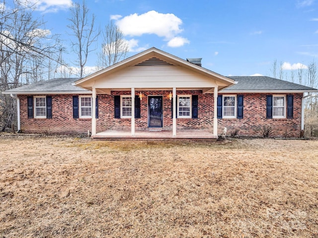 single story home with a shingled roof, a porch, a front lawn, and brick siding