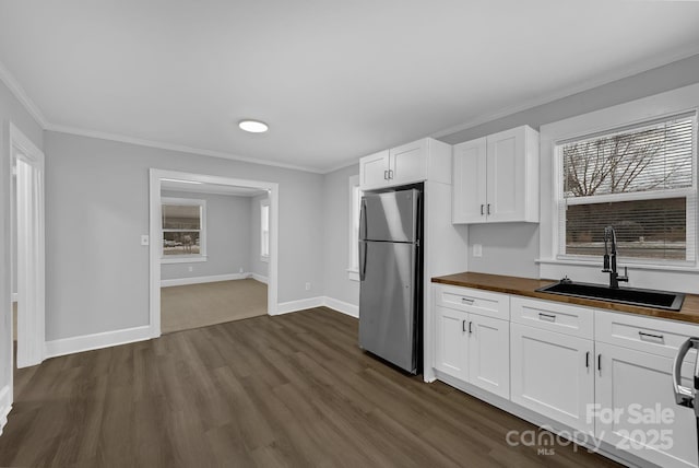 kitchen with butcher block counters, a sink, white cabinetry, freestanding refrigerator, and crown molding