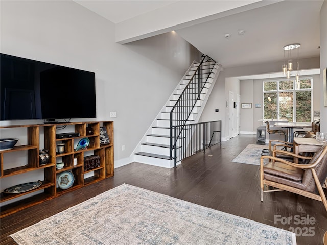 living area with dark wood-style floors, a notable chandelier, stairway, and baseboards