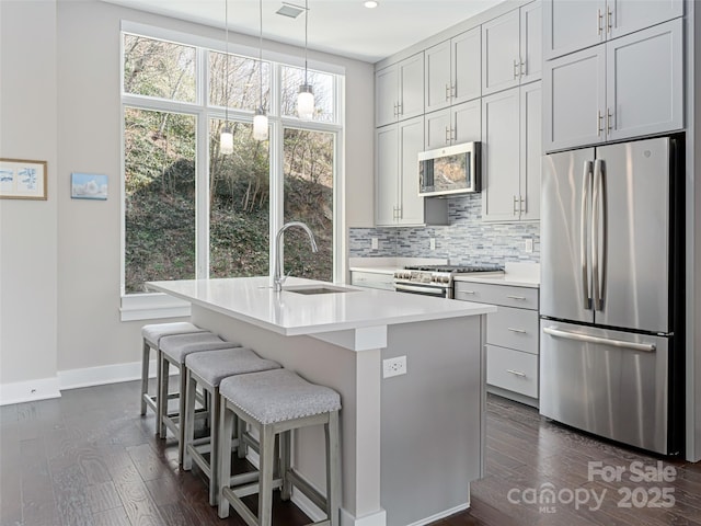 kitchen featuring light countertops, appliances with stainless steel finishes, an island with sink, and a sink