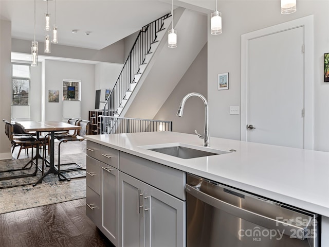 kitchen with decorative light fixtures, light countertops, gray cabinetry, stainless steel dishwasher, and a sink