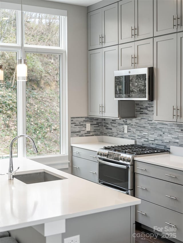 kitchen with light countertops, appliances with stainless steel finishes, a sink, and gray cabinetry