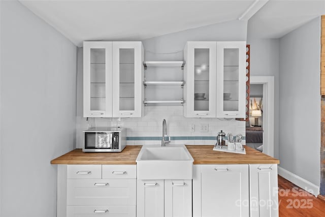 kitchen featuring a sink, stainless steel microwave, wooden counters, and backsplash