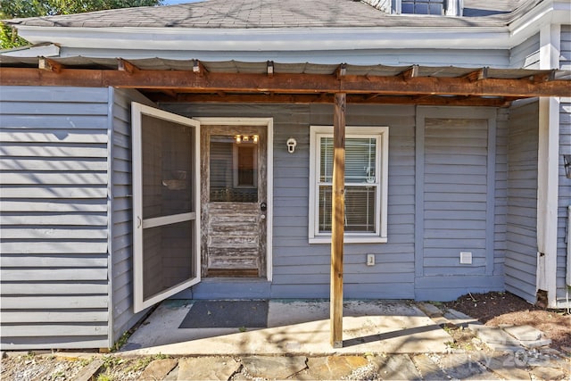 view of exterior entry with roof with shingles