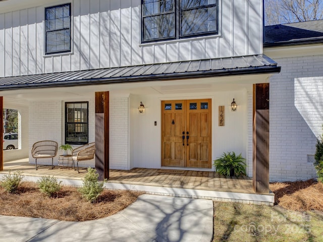 entrance to property featuring metal roof, a porch, board and batten siding, and brick siding