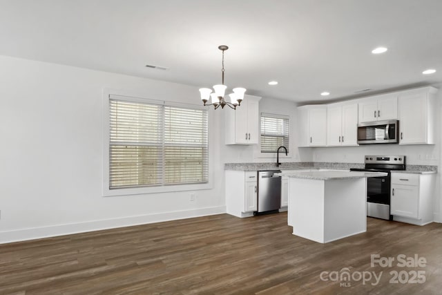 kitchen featuring white cabinets, appliances with stainless steel finishes, decorative light fixtures, and a center island