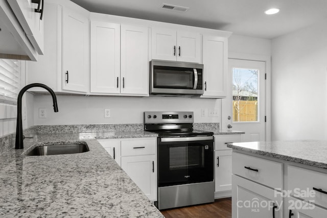 kitchen featuring stainless steel appliances, visible vents, white cabinetry, a sink, and light stone countertops