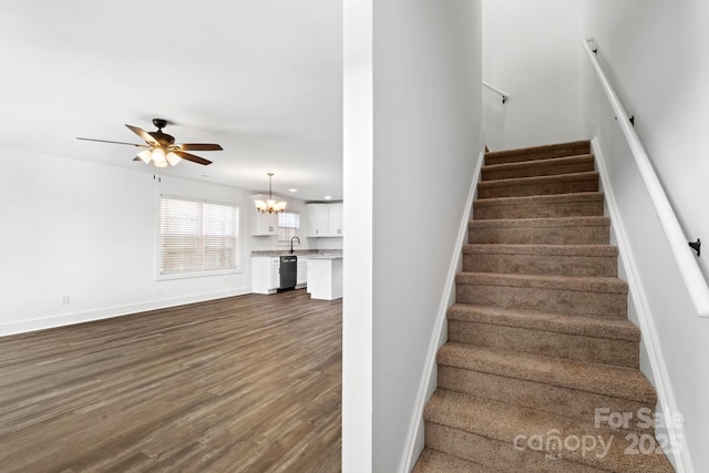 staircase featuring ceiling fan with notable chandelier, baseboards, and wood finished floors