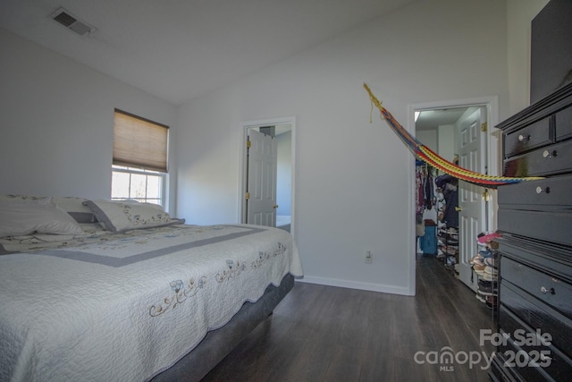 unfurnished bedroom with visible vents, baseboards, vaulted ceiling, a spacious closet, and dark wood-style floors