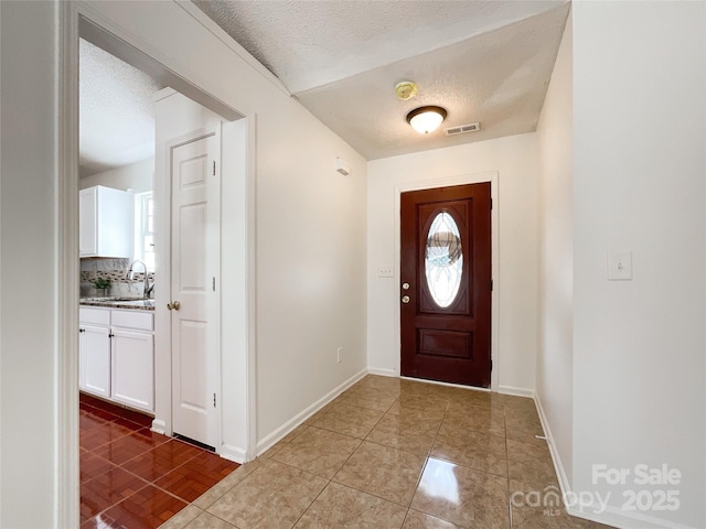 tiled entrance foyer with a textured ceiling, baseboards, visible vents, and a sink