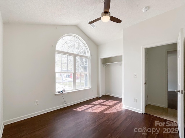 unfurnished bedroom featuring multiple windows, a textured ceiling, lofted ceiling, and wood finished floors