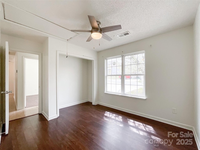 unfurnished bedroom with visible vents, dark wood-type flooring, attic access, a closet, and a textured ceiling